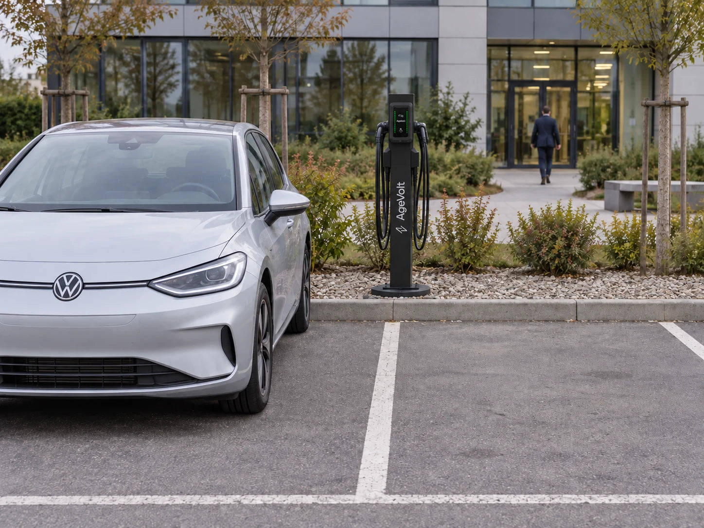 Pillar Slim s TouchPointom na okrúhlom Smart Base za obrubníkom, medzi dvoma parkovacími miestami. V susednom státí parkuje auto.